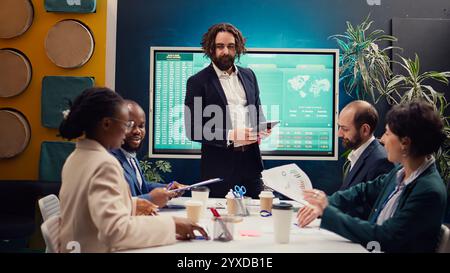 Der Projektmanager begrüßt sein Team bei einem Geschäftstreffen und schüttelt dabei die Hände. Der Vorgesetzte erläutert die allgemeinen Unternehmensziele, analysiert die aktuelle Situation und arbeitet die Planungsdetails durch. Kamera B.. Stockfoto