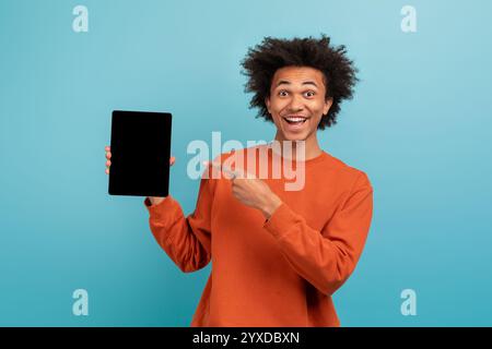 Junger Mann mit lockigem Haar zeigt Tablette auf hellblauem Hintergrund Stockfoto