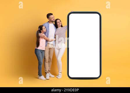 Dreiköpfige Familie mit einem Smartphone auf gelbem Hintergrund Stockfoto