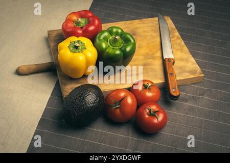 Paprika mit Tomaten und Avocado auf hölzernem Schneidebrett. Frisches Gemüse und Messer auf Holzbrett. Stockfoto