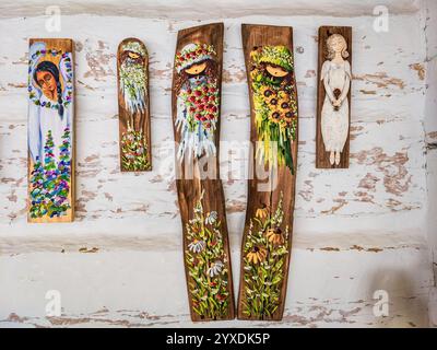 Sanok, Polen - 4. Mai 2024. Fünf handbemalte Holztafeln mit skurrilen Engeln und Blumenmädchen hängen vor einer rustikalen weißen Holzkulisse. Stockfoto