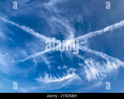 Wunderschöne Zirruswolken mit Kondensstreifen oder Dampfspuren (Homogenitus), die ein Kreuz am Himmel bilden Stockfoto