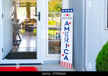 Ein amerikanisches Vorstadthaus mit offener Vordertür zeigt patriotischen Stolz mit einem Willkommensschild auf der Veranda. Stockfoto