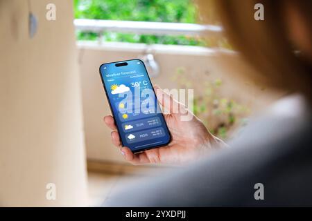 Frau auf dem Balkon, die Wettervorhersage auf ihrem Handy überprüft. Stockfoto