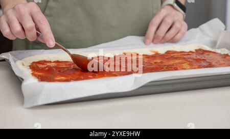 Nahaufnahme: Tomatensauce auf Pizzateig verteilen. Zubereitung traditioneller Sauce für hausgemachte Pizza. Italienisches Essen. Pizza wird hergestellt Stockfoto