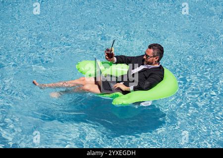 Sommerwochenende und freie Arbeit. Verrücktes Comic-Geschäft. Lustiger Geschäftsmann im Anzug mit Laptop im Sommerschwimmbad. Abgelegener Sommer Stockfoto