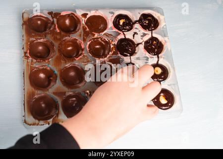 Die Hand eines Kindes steckt Nüsse in eine Form, um handgemachte Schokolade herzustellen. Hochwertige Fotos Stockfoto