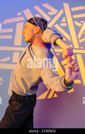 Ein junger Mann in einem Bandana tanzt gegen eine Wand mit geometrischen Mustern Stockfoto