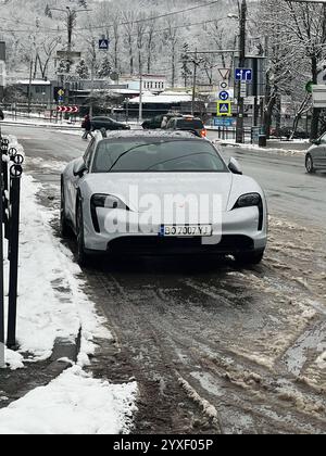 Kiew, Ukraine - 15. Dezember 2024: Graues Porsche Taycan Auto parkt im Winter auf einer verschneiten Straße in einem städtischen Gebiet. Die Gegend zeigt Schilder, Gebäude, A Stockfoto