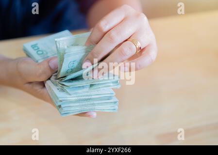 Hände, die Thailändische Badrechnungen zählen. Frauenhände halten Thai-Geld, während sie am Schreibtisch sitzen, Nahaufnahme Stockfoto
