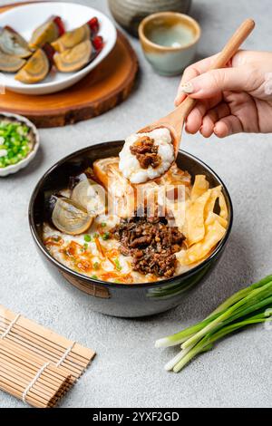 Reisbrei oder Congee mit Schweinehackfleisch, Century Ei und Kuchen in einer Schüssel Stockfoto