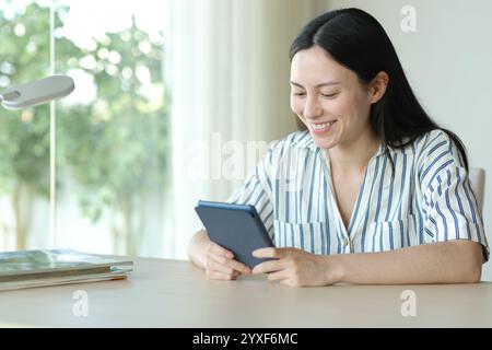 Glückliche asiatische Frau, die eBook liest, sitzt allein in einem Zimmer zu Hause Stockfoto