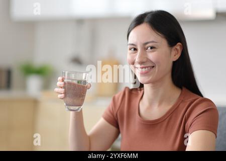 Glückliche asiatische Frau, die Wasserglas in der Küche zu Hause zeigt Stockfoto