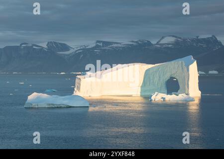 Große Eisberge im Atlantik, Eisfjord in Greenlandund der silhouettenreiche Berggrat im Hintergrund unter blauen schmelzenden Eisbergen Stockfoto