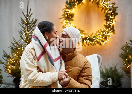 Ein wunderschönes Paar teilt sich einen freudigen Moment im Freien, umgeben von Weihnachtsbeleuchtung und Dekoration. Stockfoto