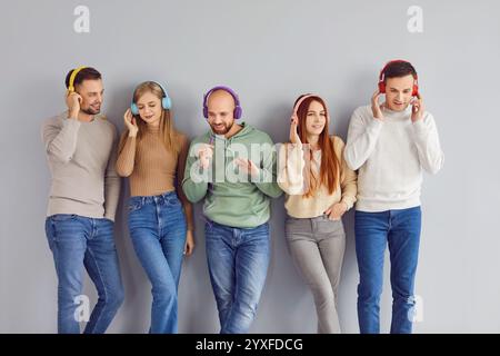 Junge glückliche Menschen, die Musik in Kopfhörern hören, tragen legere Kleidung auf grauem Hintergrund. Stockfoto