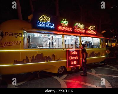 Baku, Aserbaidschan - 3. Mai 2019: Ein lebhafter Street Food Truck in Baku, der Balik Ekmek, Burger, Döner und Hot Dogs bietet, beleuchtet durch bunte Neonschilder, die Besucher anziehen Stockfoto