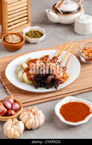 Schweinefleisch Satay oder Sate Babi. Schweinesatay serviert mit Erdnusssauce und Scheiben von Lontong oder Ketupat (Reiskuchen) Stockfoto