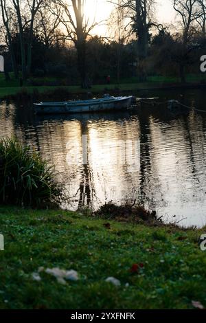 Blick auf den Sonnenuntergang über das ruhige Wasser im Bois de Vincennes Park, der ein kleines Boot hervorhebt, das ruhig zwischen den Reflexen driftet Stockfoto