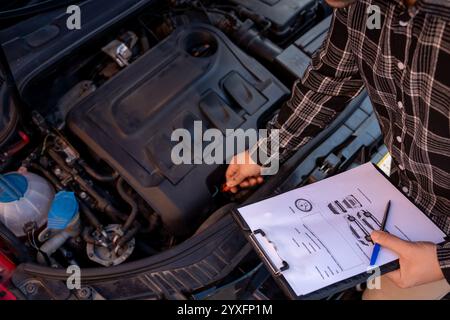 Fahrzeugmechaniker überprüft den Motorölstand und vergleicht ihn mit den Daten in der Zwischenablage Stockfoto