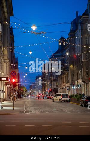 Eine pulsierende Stadtstraße in Riga, Lettland, beleuchtet von hängenden Lichtern in der Abenddämmerung. Stockfoto