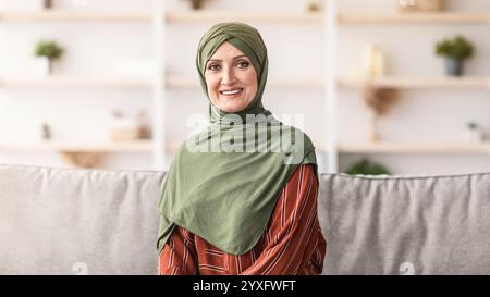 Glücklich Reif Muslimische Frau Trägt Hijab Sitzen Auf Sofa Im Innen Stockfoto