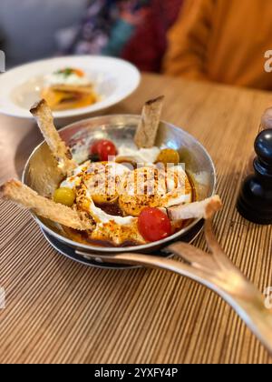 Türkische Eier oder Cilbir werden mit griechischem Joghurt kombiniert mit frischen Kräutern und Knoblauch in der Nähe auf dem Teller auf dem Holztisch zubereitet Stockfoto