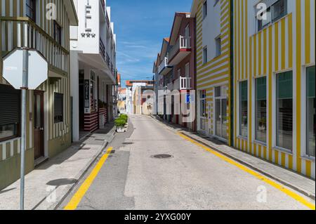 Costa Nova, Portugal - 11. September 2024 : Ein sonniger Tag offenbart eine ruhige Straße mit lebhaften gestreiften Gebäuden und blauem Himmel. Stockfoto