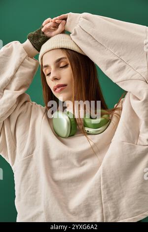 Eine junge Frau mit langen Haaren, die einen Strickmütze und einen übergroßen Pullover trägt, hört der Musik nachdenklich zu. Stockfoto