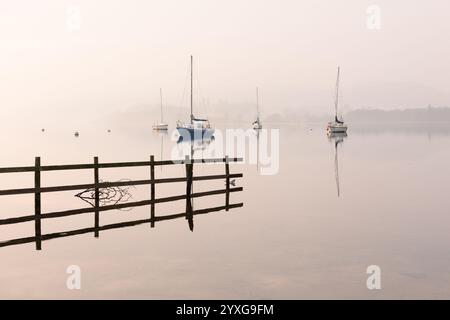 Wunderschöner ruhiger, nebeliger Morgen mit Segelbooten, die sich im See von Windermere im Lake District, Großbritannien, spiegeln. Stockfoto
