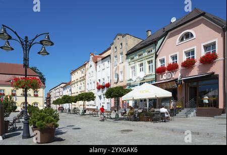 Bunte Häuserreihe in einer sonnigen Straße mit Cafés und Menschen, Blumen schmücken die Balkone, unter blauem Himmel Häuser auf dem Marktplatz, Darlo Stockfoto