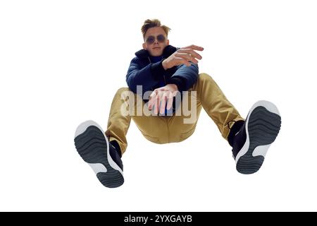 Unteransicht eines modischen jungen Mannes mit Sonnenbrille, blauer Jacke und Senfhose in dynamischer Pose. Urbaner Stil, modern, trendig Stockfoto