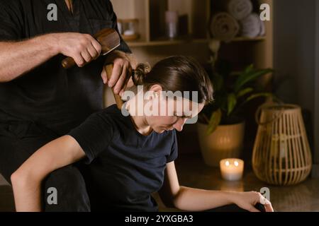 Männlicher Meister gibt Thai-Toksen-Massage für Mädchen im Massageraum. Ein Mädchen bekommt eine entspannende Thai-Rückenmassage mit einem Toxen-Massage-Set. Stockfoto