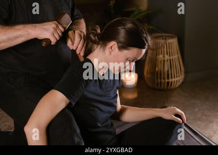 Männlicher Meister gibt Thai-Toksen-Massage für Mädchen im Massageraum. Ein Mädchen bekommt eine entspannende Thai-Rückenmassage mit einem Toxen-Massage-Set. Stockfoto