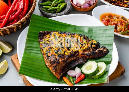 Ikan Pari Bakar oder gegrillter Sting Ray in Chili-Currysauce serviert auf Bananenblatt mit Schalotten, Gurke und Chili. Stockfoto