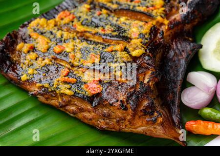 Ikan Pari Bakar oder gegrillter Sting Ray in Chili-Currysauce serviert auf Bananenblatt mit Schalotten, Gurke und Chili. Stockfoto