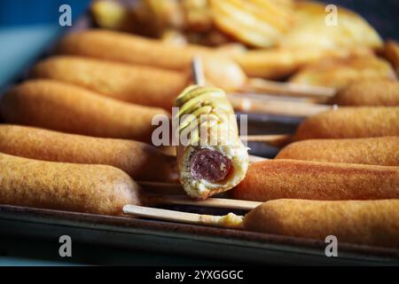 Pfanne voller Maishunde, einer mit Senf und Pommes im Hintergrund. Selektiver Fokus mit unscharfem Hintergrund. Stockfoto