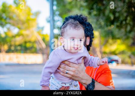 Ein fröhlicher Vater wirft seine kleine Tochter während eines sonnigen Familienausflugs hoch in die Luft und feiert Liebe, Verspieltheit und die kostbare Bindung der Eltern Stockfoto