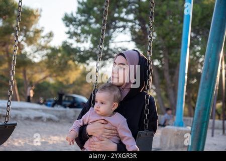 Ein herzerwärmender Moment, in dem eine muslimische Mutter im traditionellen Abaya- und Hijab-Stil gefangen wird, die Freude am Spielplatz mit ihrem Baby teilt und kulturelle vielfalt miteinander verbindet Stockfoto