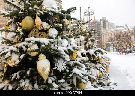 Geschmückter Weihnachtsbaum auf der Straße der Stadt. Schneebedeckte Zweige Schnee. Wunderschöne goldene Spielzeuge auf dem Weihnachtsbaum. Weihnachten, Neujahr. Einrichtung Stockfoto