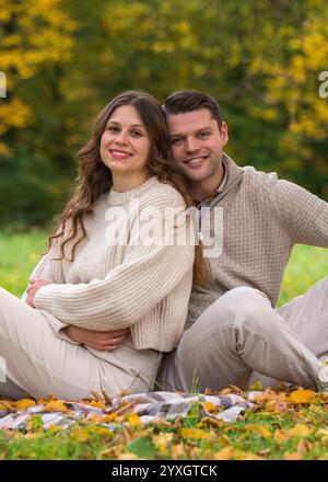 Junges, unbeschwertes, schönes Paar, das am Herbsttag im Park auf einer Decke sitzt, lacht und sich gegenseitig Gesellschaft genießt. Liebe, glückliche Familie. Stockfoto