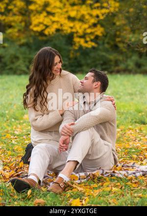 Junges, unbeschwertes, schönes Paar, das am Herbsttag im Park auf einer Decke sitzt, lacht und sich gegenseitig Gesellschaft genießt. Liebe, glückliche Familie. Stockfoto