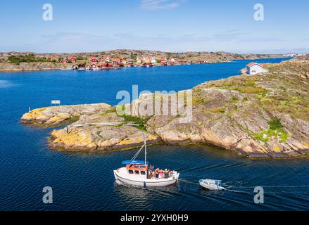 Eine Familie in einem kleinen Fischerboot segelt zwischen den unzähligen bewohnten Inseln mit typisch rot bemalten Häusern der Touristenprovinz Bohuslän. Stockfoto