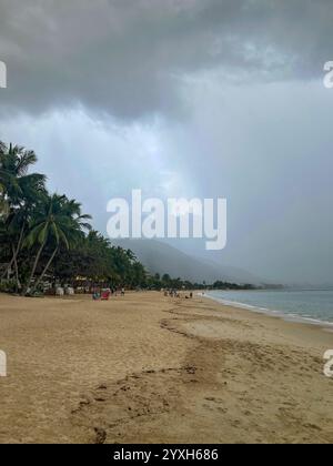 Starke Regenwolken nähern sich Lamai Beach mit nebeliger Bergkulisse, Palmen am Sandstrand und Strandbesucher entlang der Küste Stockfoto