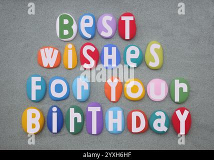 BEST wishes for your birthday, kreativer Festtext mit mehrfarbigen, handbemalten Steinbuchstaben über grünem Sand Stockfoto