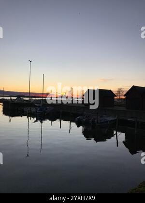 Sonnenuntergang hinter Bootshäusern und Reflexionen im Wasser an einem kleinen Hafen in Västerås, Schweden. Foto im Oktober 2022. Stockfoto