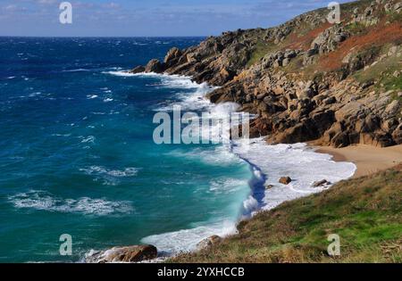 Am Porth Chapel Beach in der Nähe des Minack Theaters in West Penwith, Cornwall, stürzen Wellen auf die abfallenden Klippen und den Sand Stockfoto