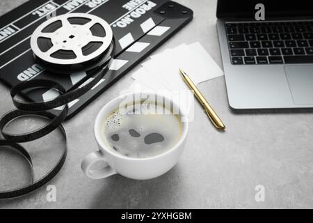 Tasse Kaffee, Filmklatscher, Filmrolle und Laptop auf grauem, strukturiertem Tisch Stockfoto