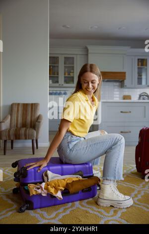 Glückliche überglückte Touristenfrau, die auf überladenem Reisekoffer sitzt Stockfoto
