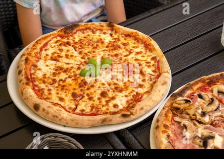 Nahaufnahme von Margherita Pizza auf einem Restauranttisch mit Basilikumgarnitur, köstliche authentische italienische Küche, Holzofenpizza, Essen im Freien, ph-wert Stockfoto